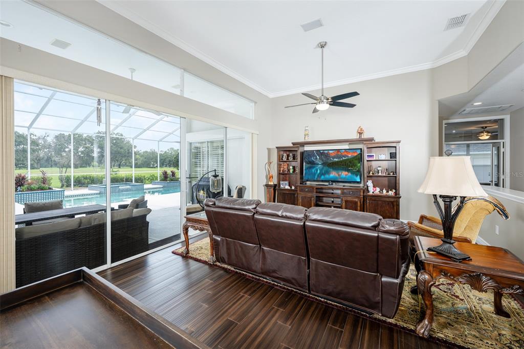 A living room with dark wood floors, a leather sofa, and sliding doors overlooking a pool — 5429 BURNT HICKORY DRIVE, VALRICO, FL