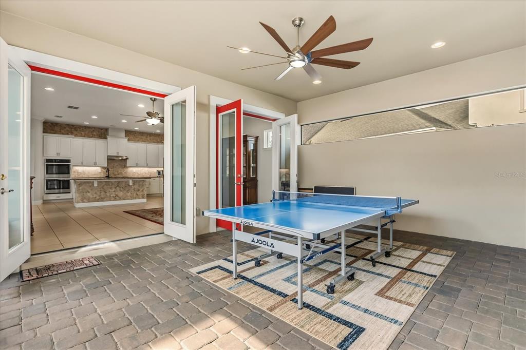 A covered porch features brick pavers, two dark wicker chairs, and a bright red double door — 12837 BOVET AVENUE, ORLANDO, FL