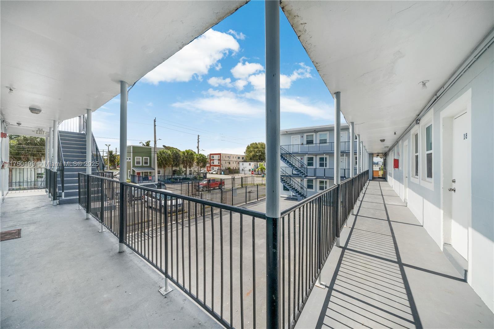 An outdoor walkway with metal railings overlooks a parking lot between two apartment buildings — 1281 NW 61st St # 2, Miami FL 33142, MIAMI, FL