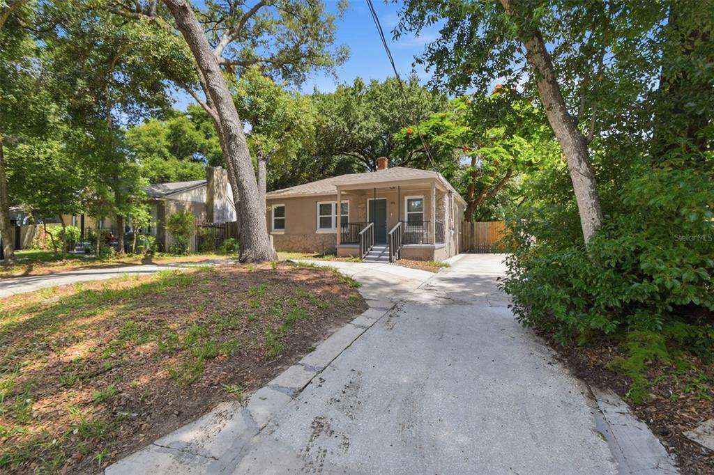 A single-story house with a covered front porch and a concrete driveway sits among trees — 1416 E MOHAWK AVENUE, TAMPA, FL