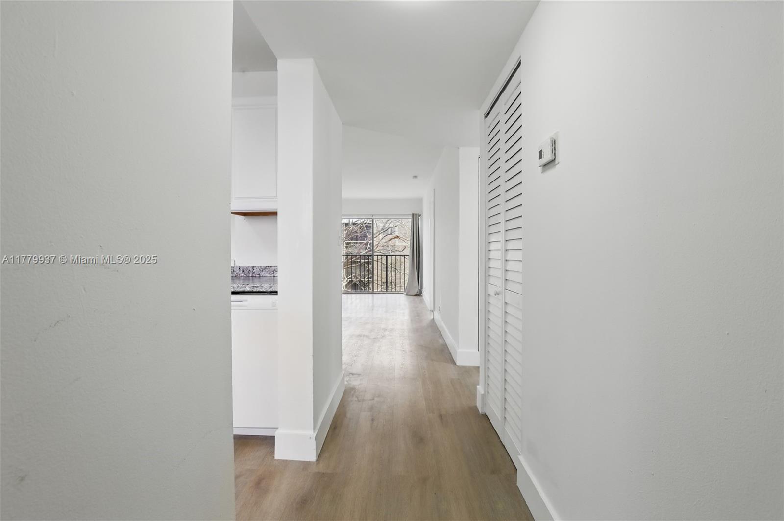 A hallway with light wood flooring leads past a kitchen toward a balcony with trees — 8540 N Sherman Cir # 408, Miramar FL 33025, MIRAMAR, FL