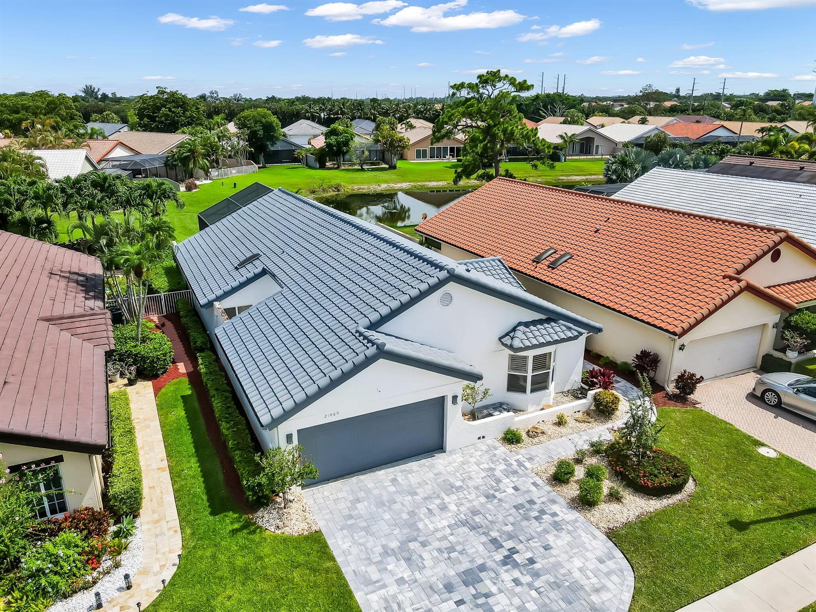 An aerial view shows a white house with a blue tile roof and paver driveway — 21089 Cottonwood Drive, Boca Raton FL 33428, BOCA RATON, FL