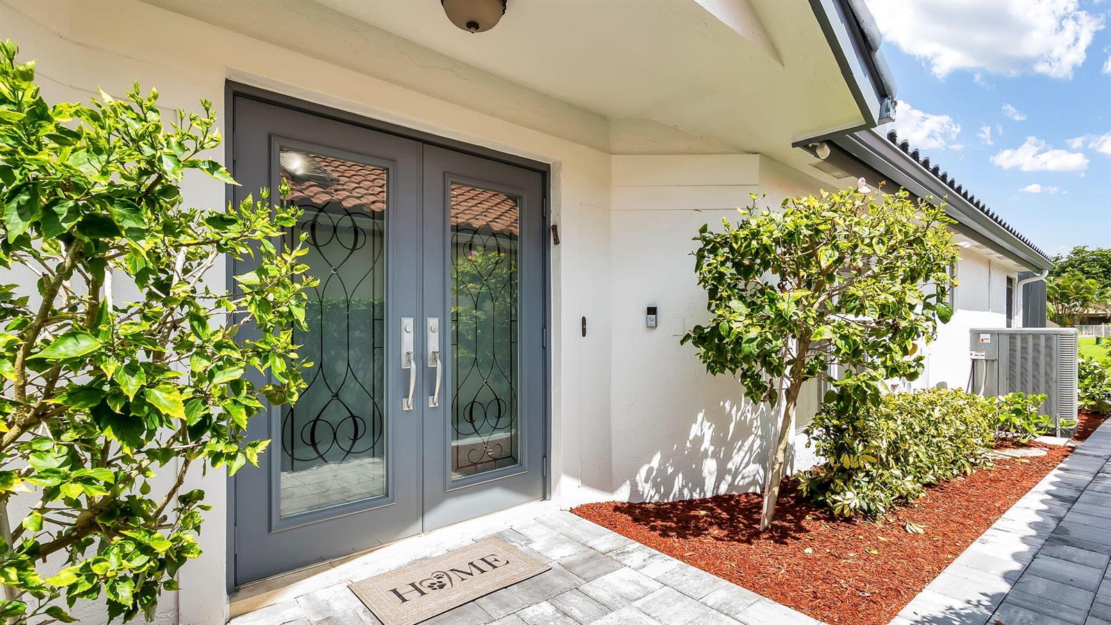 A gray double front door with glass inserts sits on a paved porch with landscaping — 21089 Cottonwood Drive, Boca Raton FL 33428, BOCA RATON, FL