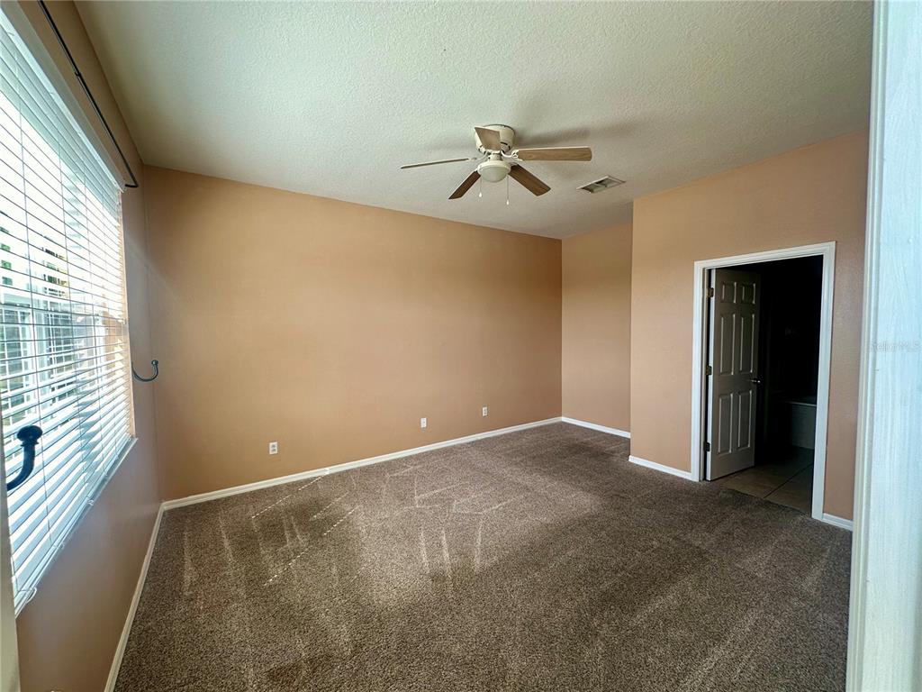 An empty bedroom features tan walls, brown carpeting, a ceiling fan, and a window — 6112 CHAPLEDALE DRIVE, ORLANDO, FL