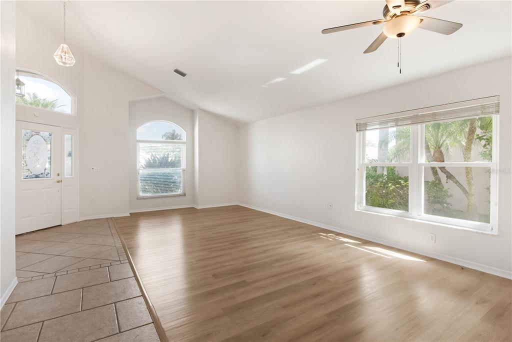 A bright living room features light wood flooring, white walls, a ceiling fan, and windows — 6801 SUPERIOR STREET CIRCLE, SARASOTA, FL