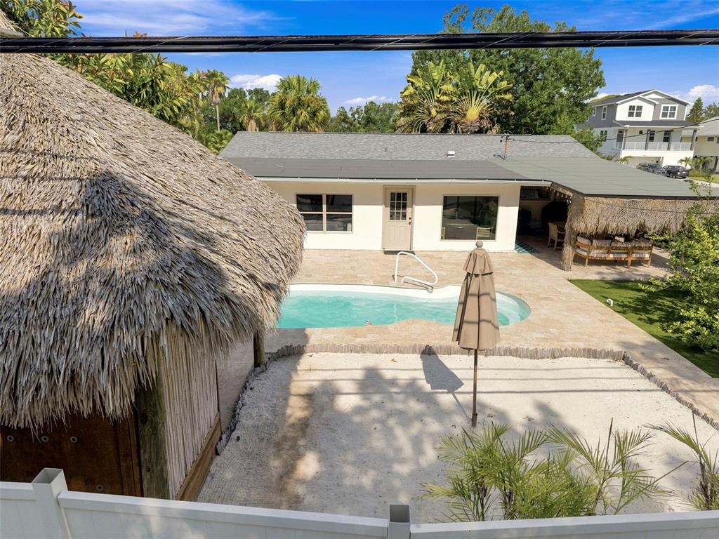 An outdoor backyard features a swimming pool, a tiki hut, and a covered patio area — 3947 HUNTINGTON STREET NE, ST PETERSBURG, FL