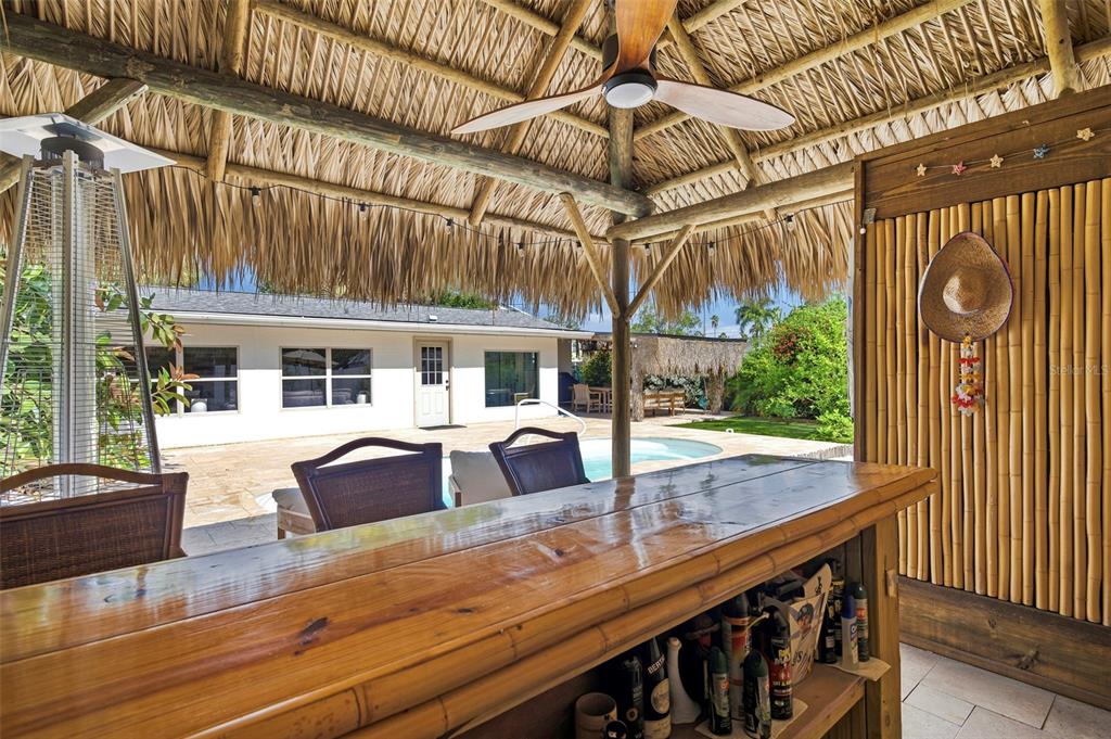 A tiki bar with a thatched roof overlooks a backyard pool and patio area — 3947 HUNTINGTON STREET NE, ST PETERSBURG, FL