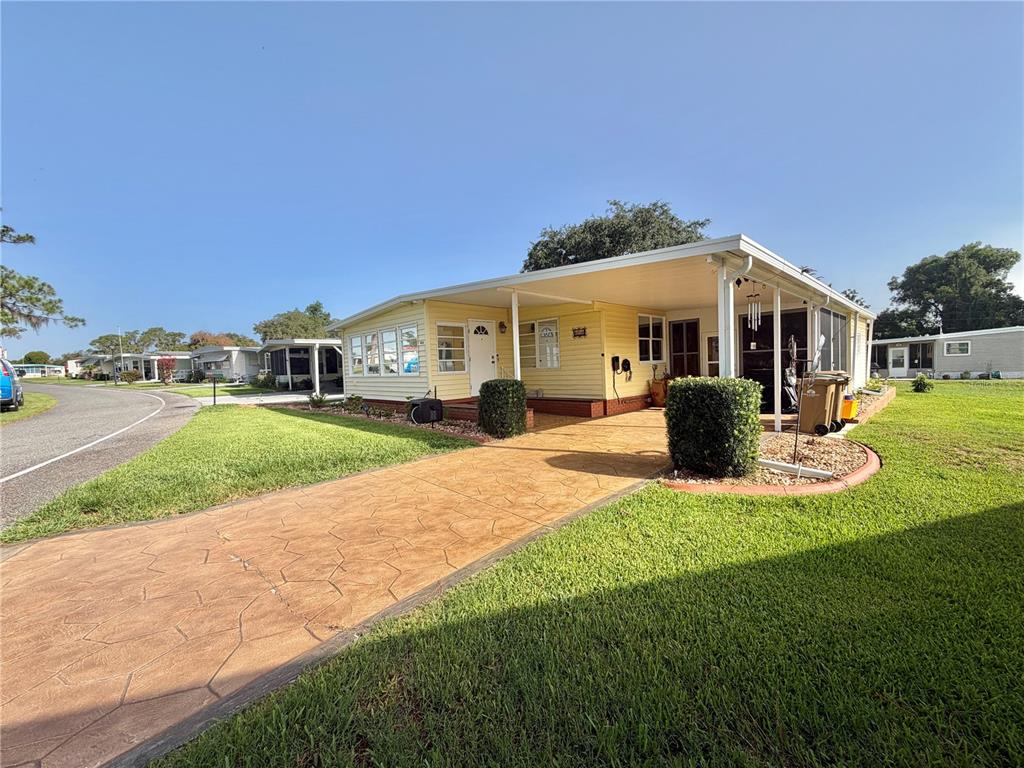 A yellow manufactured home with a covered carport and a stamped concrete driveway — 416 PALO VERDE DRIVE, LEESBURG, FL