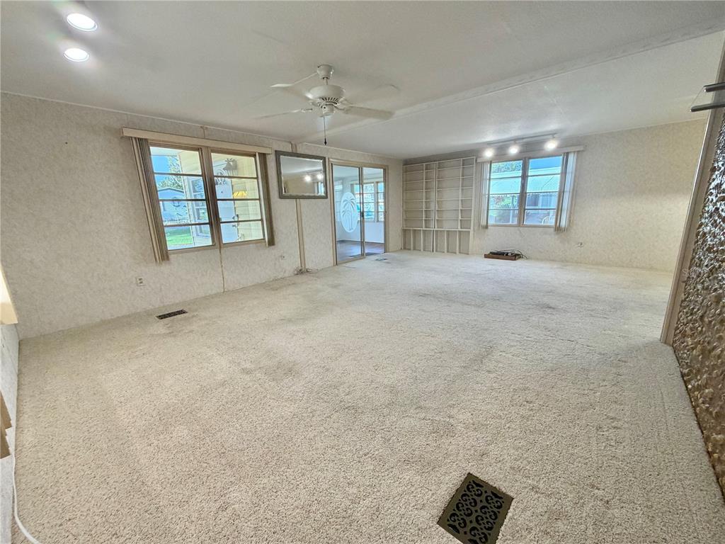 A spacious living room features beige carpeting, white paneled walls, a ceiling fan, and shelving — 416 PALO VERDE DRIVE, LEESBURG, FL