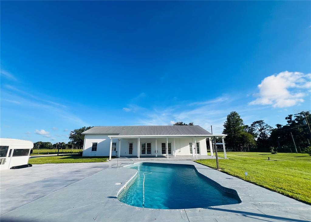 A white house with a metal roof sits behind a swimming pool on a lawn — 9120 COUNTY ROAD 304, BUNNELL, FL