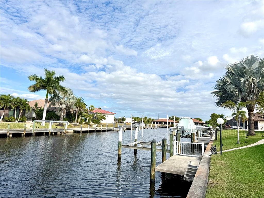 A canal view featuring boat docks, palm trees, and residential homes under a cloudy sky — 2736 MAGDALINA DRIVE, PUNTA GORDA, FL