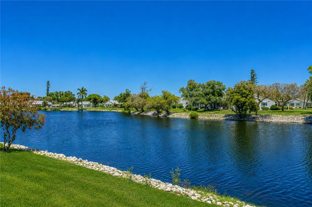 A grassy lawn borders a pond with a stone edge and houses in the background — 4603 LEXINGTON CIRCLE, BRADENTON, FL