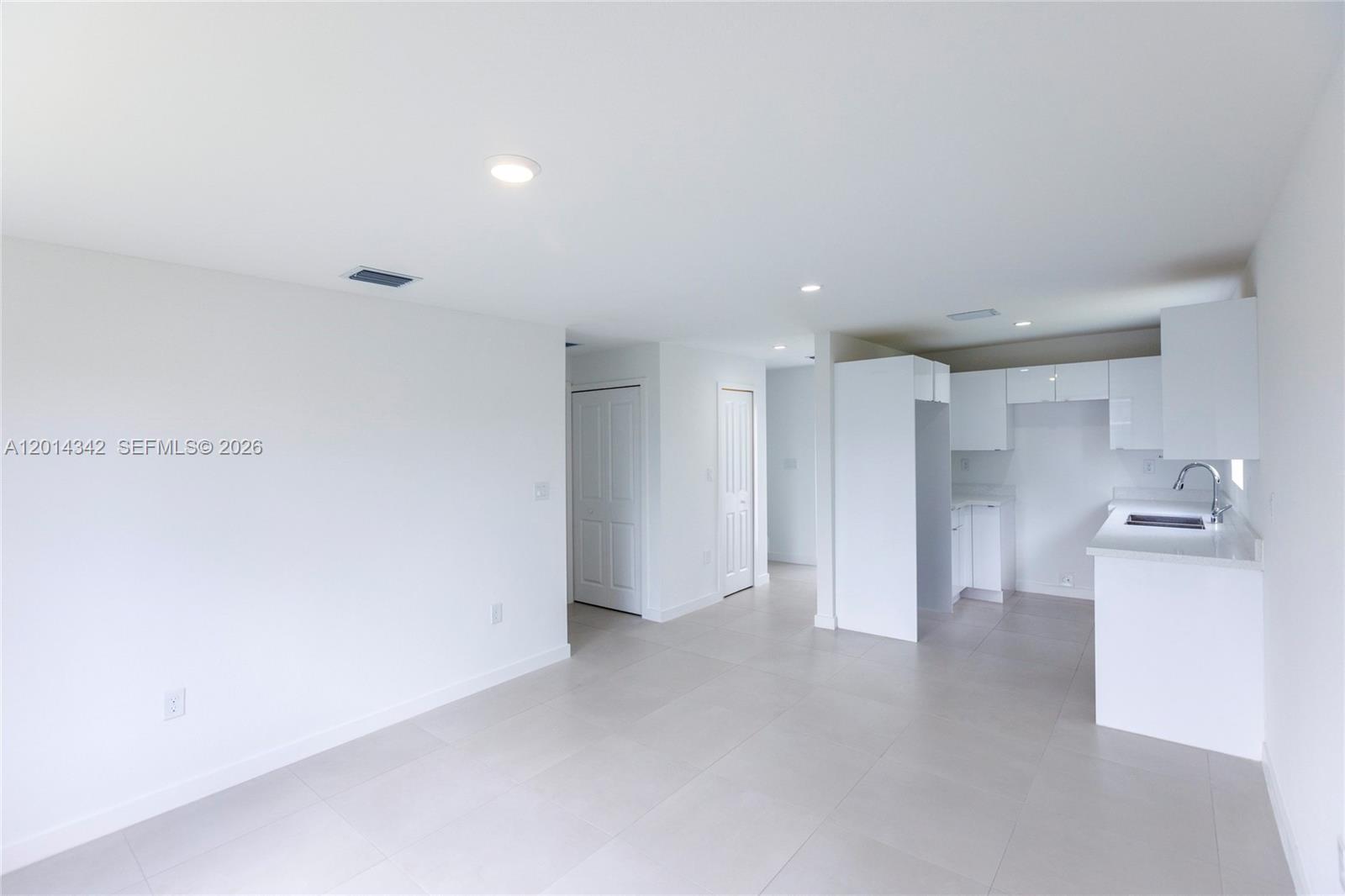 A bright, minimalist kitchen and living area features white cabinetry, light tile flooring, and recessed lighting — 9155 NW 32 Ave, Miami FL 33147, MIAMI, FL