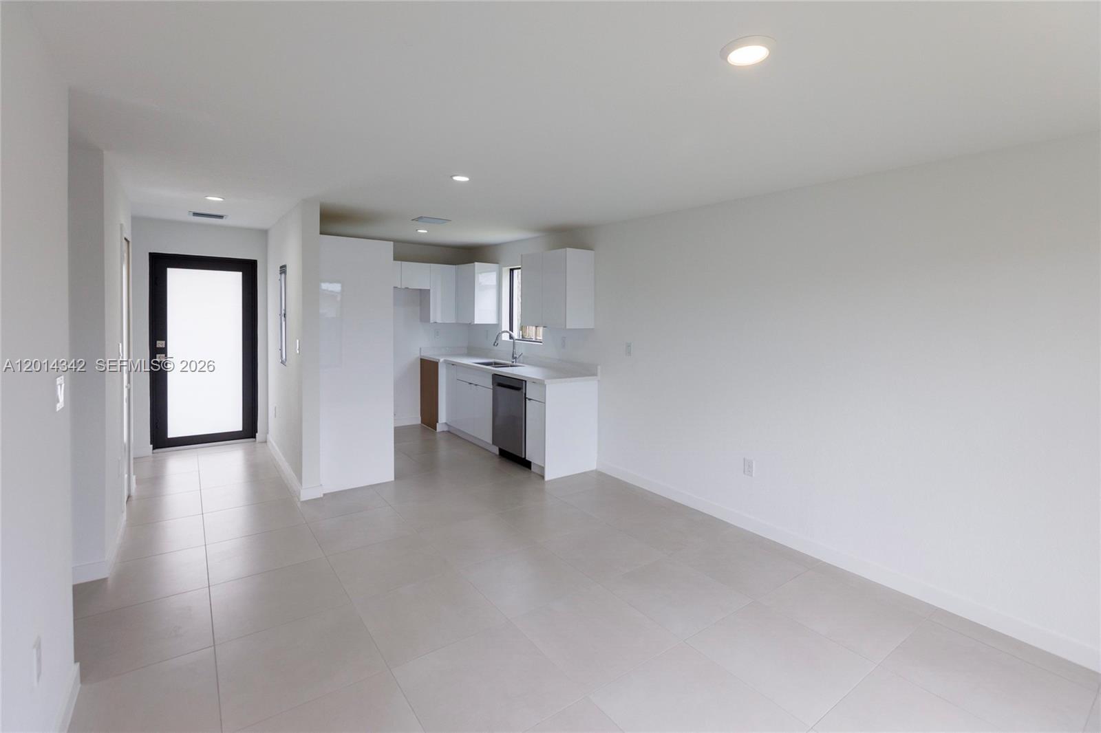 A minimalist kitchen with white cabinets and light tile floors opens into a living area — 9155 NW 32 Ave, Miami FL 33147, MIAMI, FL