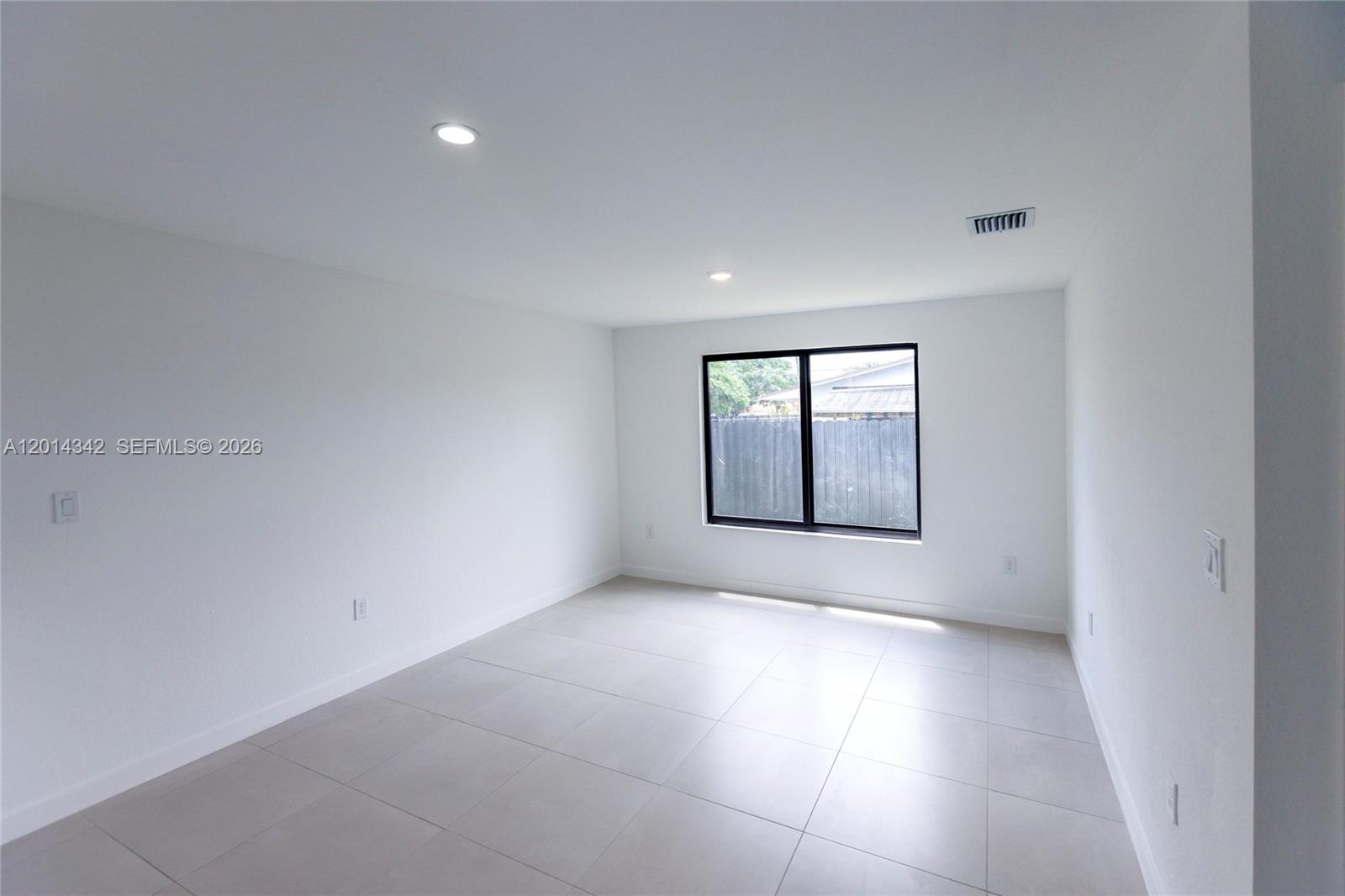 A bright, empty room features white walls, large light-colored floor tiles, and a black-framed window — 9155 NW 32 Ave, Miami FL 33147, MIAMI, FL