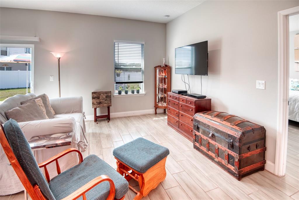 A living room features light-colored tile flooring, a television mounted above a wooden dresser, and furniture — 125 INCONNU COURT, KISSIMMEE, FL