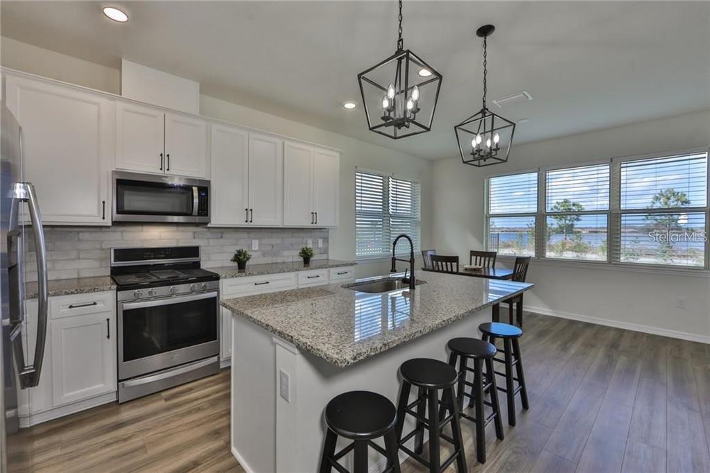 A modern kitchen features white cabinets, granite countertops, a center island, and stainless steel appliances — 3323 MONROE MEADOWS DRIVE, ODESSA, FL