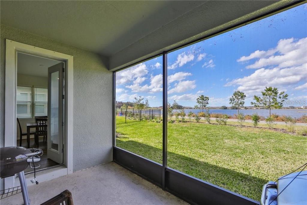 A screened-in porch overlooks a grassy backyard and a lake under a blue sky — 3323 MONROE MEADOWS DRIVE, ODESSA, FL