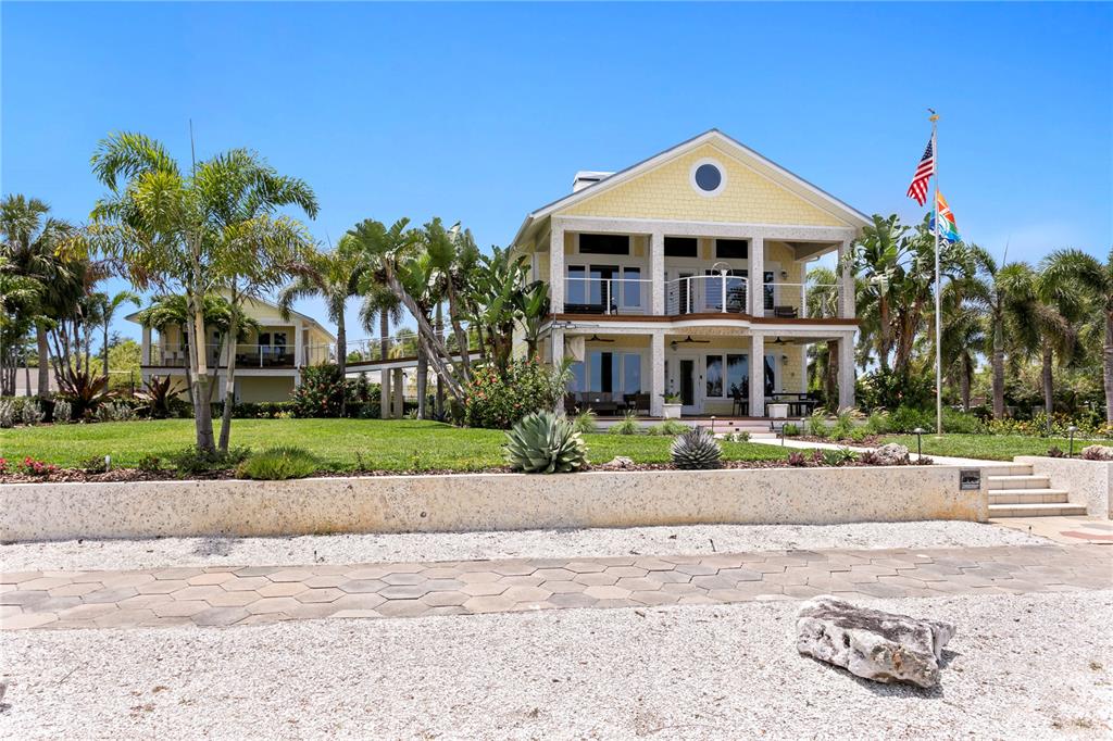 A two-story yellow house with a covered porch sits behind a stone retaining wall — 1803 BEACH DRIVE SE, ST PETERSBURG, FL