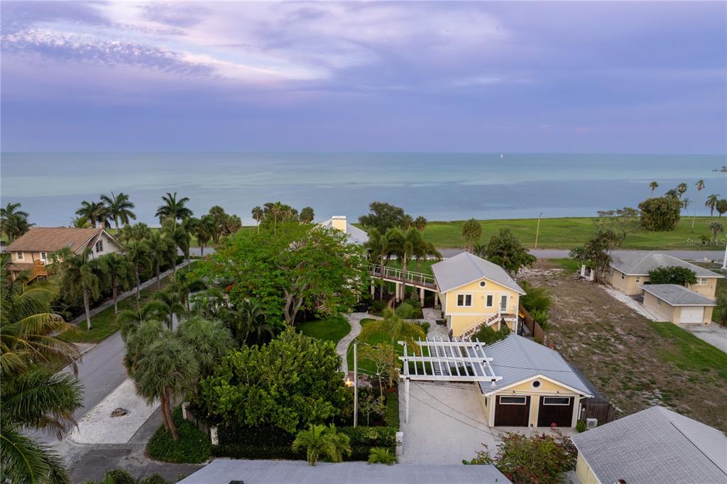 An aerial view shows a coastal property with a yellow house, lush landscaping, and ocean views — 1803 BEACH DRIVE SE, ST PETERSBURG, FL