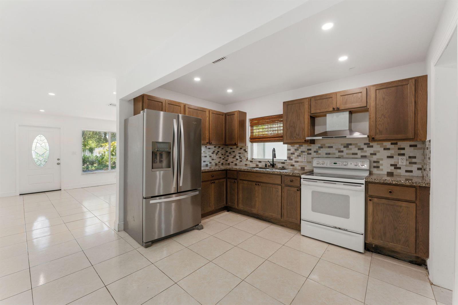 A kitchen features wood cabinets, stainless steel appliances, a white stove, and light tile flooring — 441 NW 1st Way, Deerfield Beach FL 33441, DEERFIELD BEACH, FL