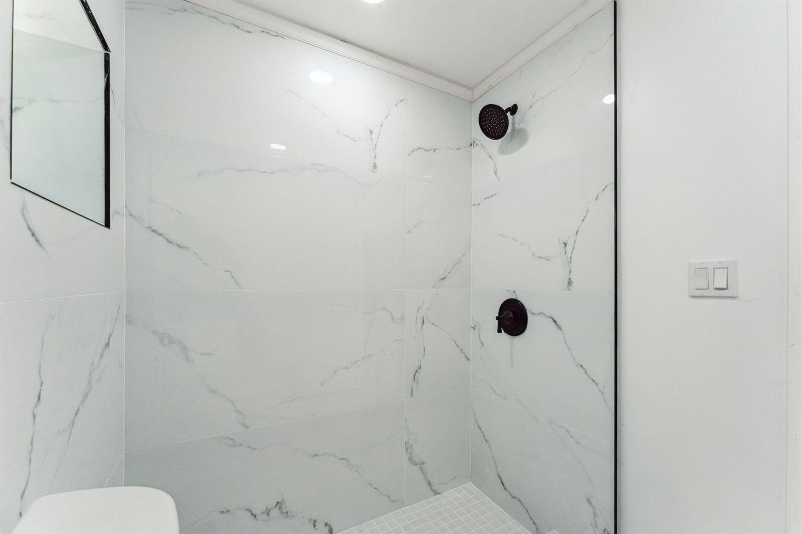 A walk-in shower features white marble-look wall tiles, black fixtures, and a white tiled floor — 441 NW 1st Way, Deerfield Beach FL 33441, DEERFIELD BEACH, FL