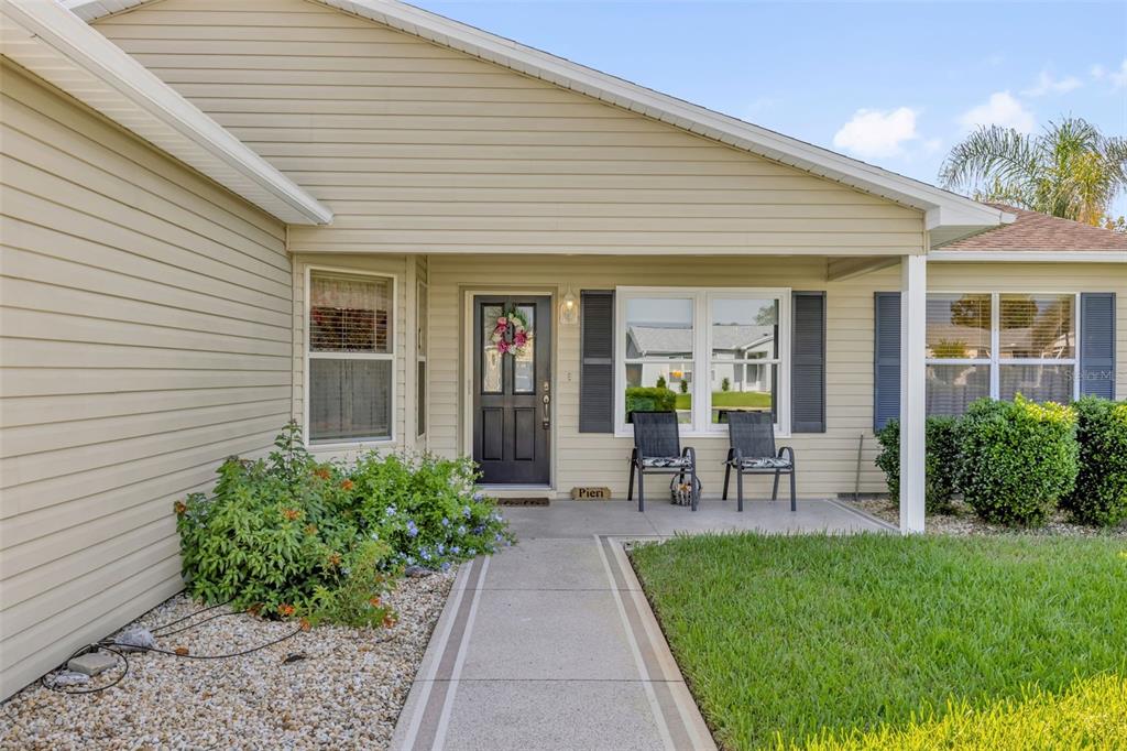 A beige-sided house exterior features a concrete walkway leading to a covered front porch — 1707 GOMEZ PLACE, THE VILLAGES, FL