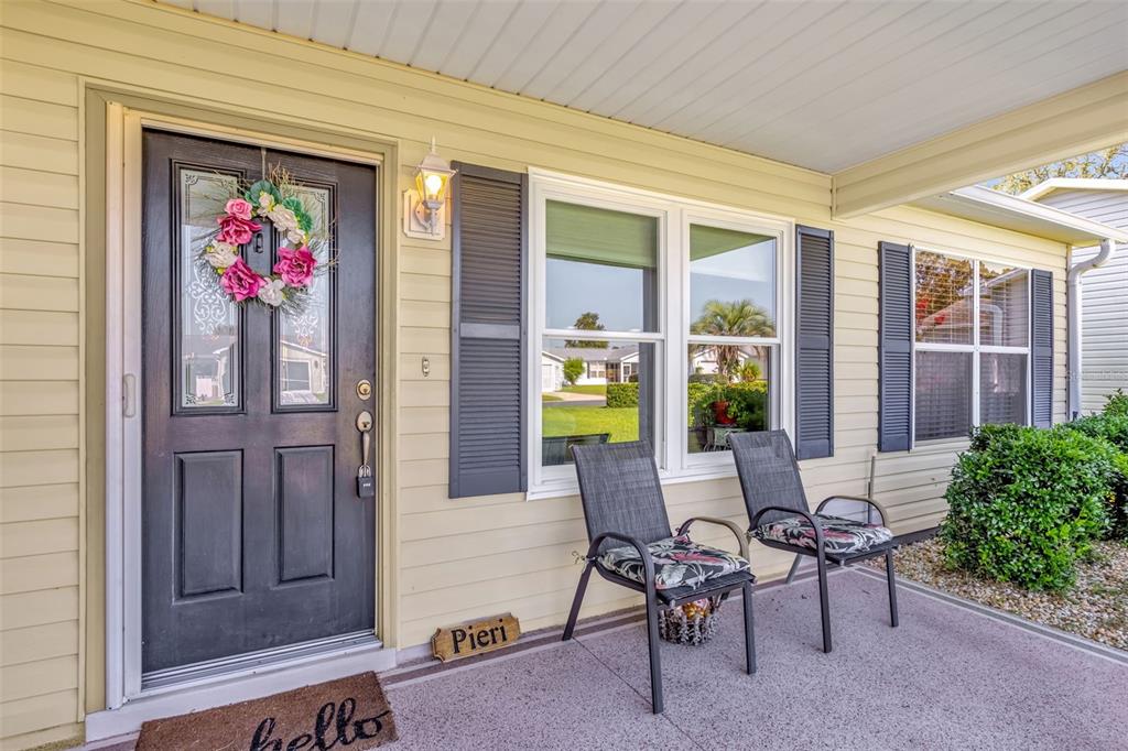 A front porch features a dark door with a wreath, two chairs, and light siding — 1707 GOMEZ PLACE, THE VILLAGES, FL