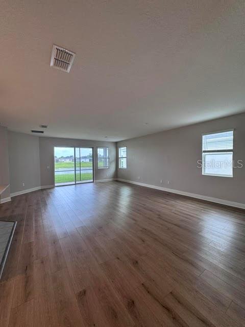 An empty living room features light wood-look flooring, neutral walls, and a sliding glass door — 3550 74TH AVENUE CIRCLE E, SARASOTA, FL