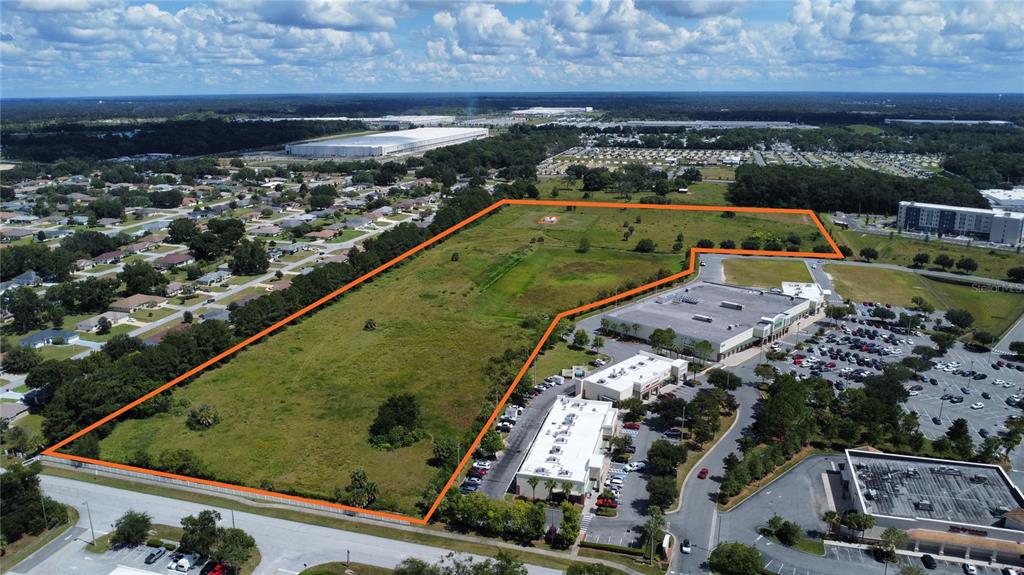 An aerial view shows a large, undeveloped grassy lot outlined in orange next to commercial buildings — 2785 NW 49TH AVENUE, OCALA, FL