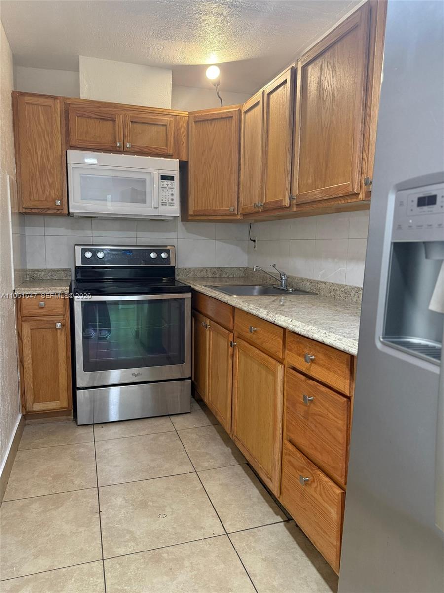 A kitchen features wood cabinets, stainless steel appliances, and granite countertops over tile flooring — 4805 NW 7th St # 15, Miami FL 33126, MIAMI, FL
