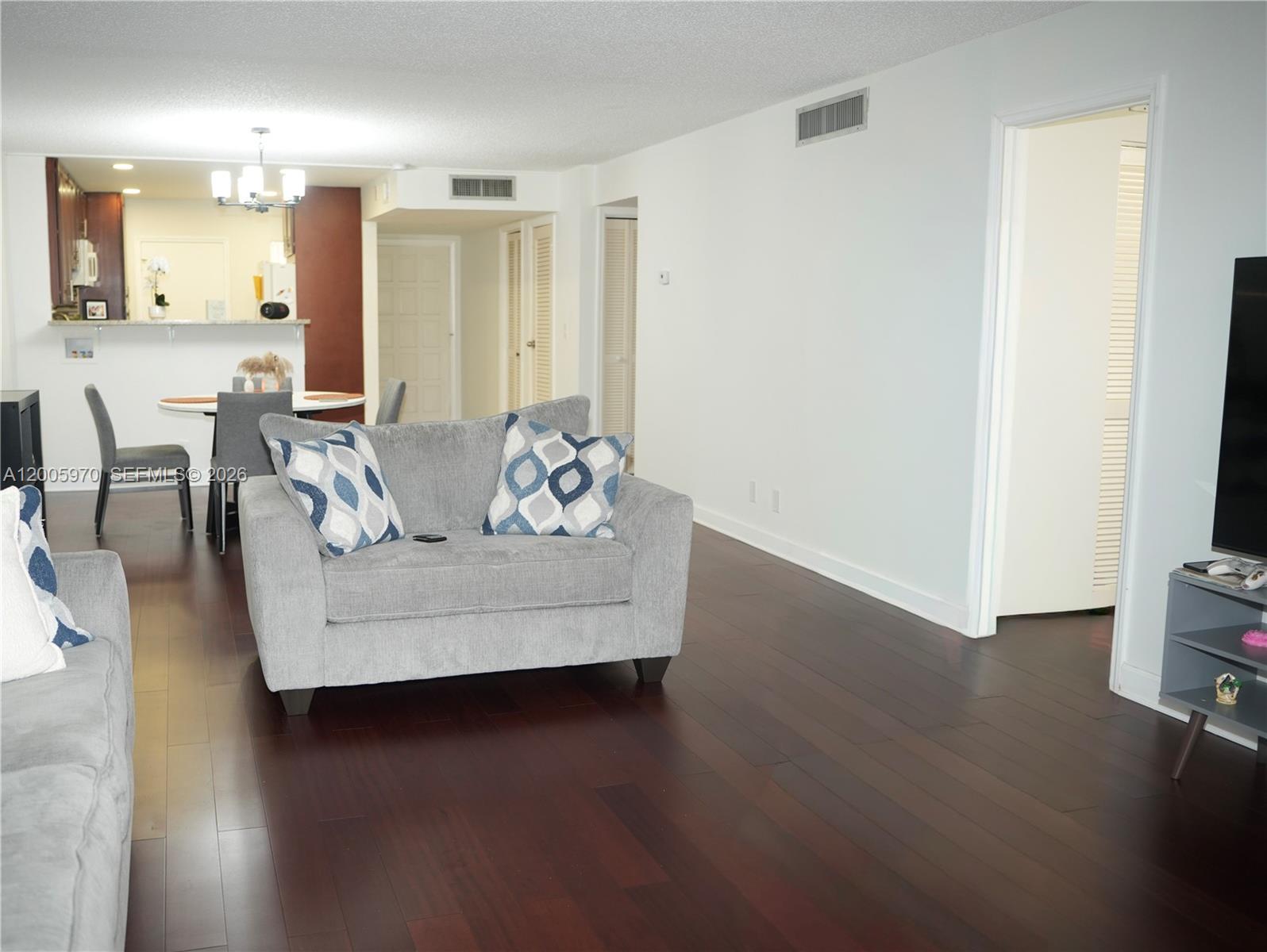 A living room with dark wood floors, gray furniture, and an adjacent dining area — 6001 N Falls Cir Dr # 203, Lauderhill FL 33319, LAUDERHILL, FL