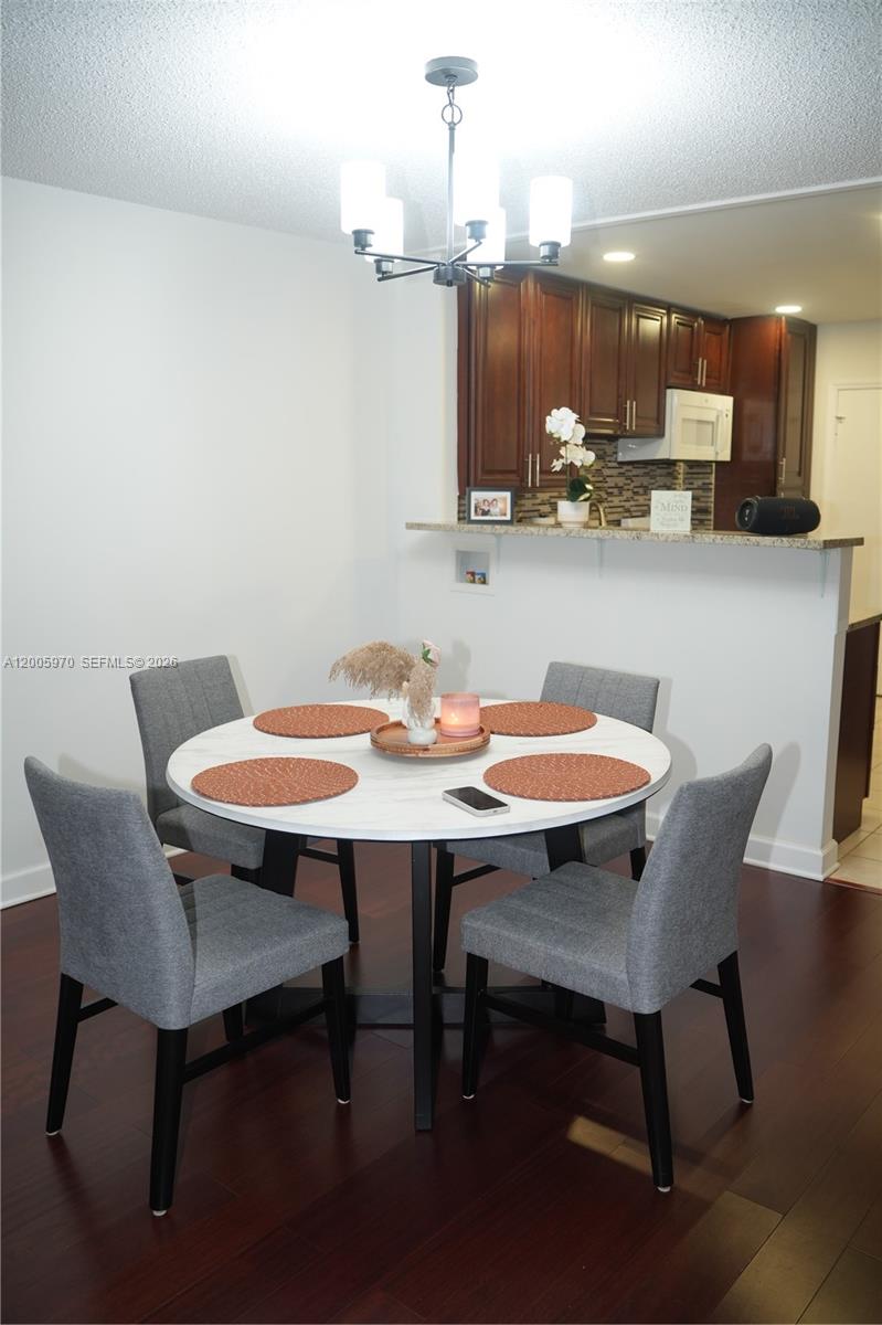 A dining area features a round white table with four gray chairs under a chandelier — 6001 N Falls Cir Dr # 203, Lauderhill FL 33319, LAUDERHILL, FL