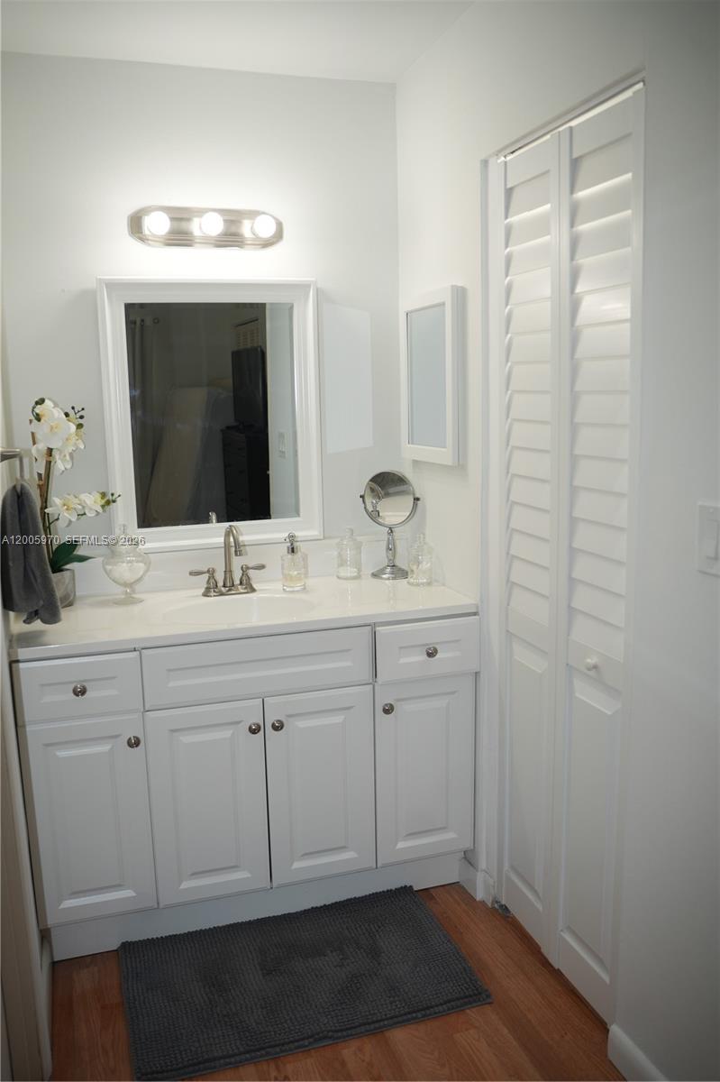 A white bathroom vanity with a mirror, sink, and louvered closet doors on wood flooring — 6001 N Falls Cir Dr # 203, Lauderhill FL 33319, LAUDERHILL, FL