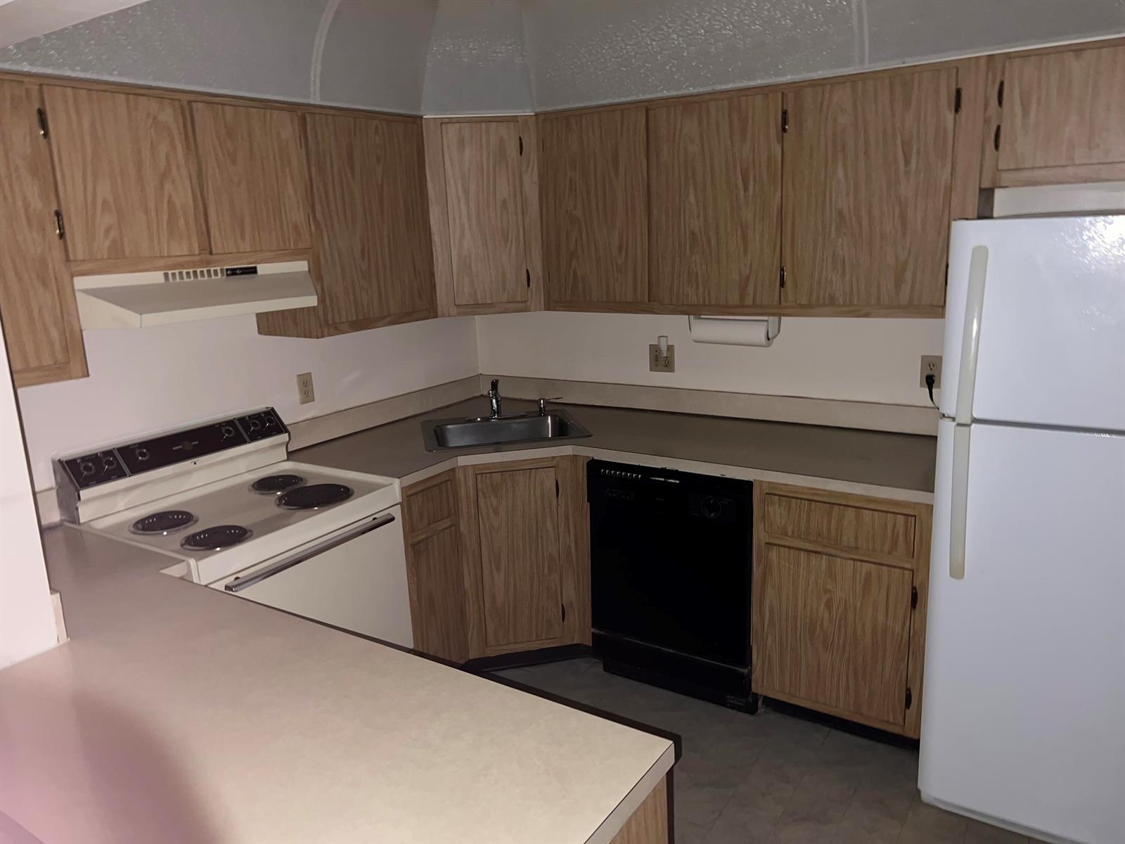A kitchen features wood cabinets, white appliances, a corner sink, and a laminate countertop — 414 Pine Glen Lane # 1, FL 33463, FL