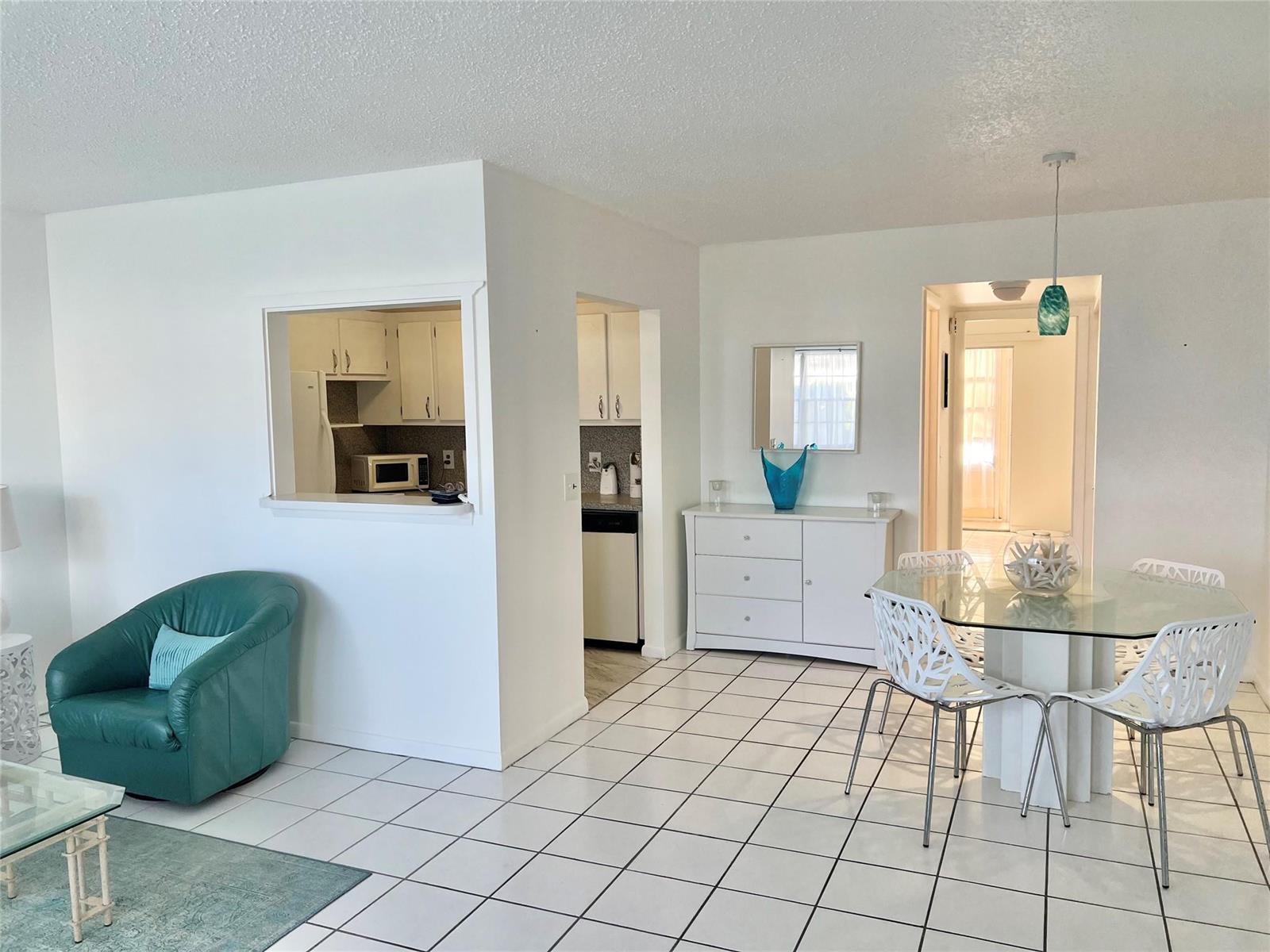 A dining area with a glass table and white chairs sits adjacent to a kitchen pass-through — 266 Oakridge P # 266, Deerfield Beach FL 33442, DEERFIELD BEACH, FL