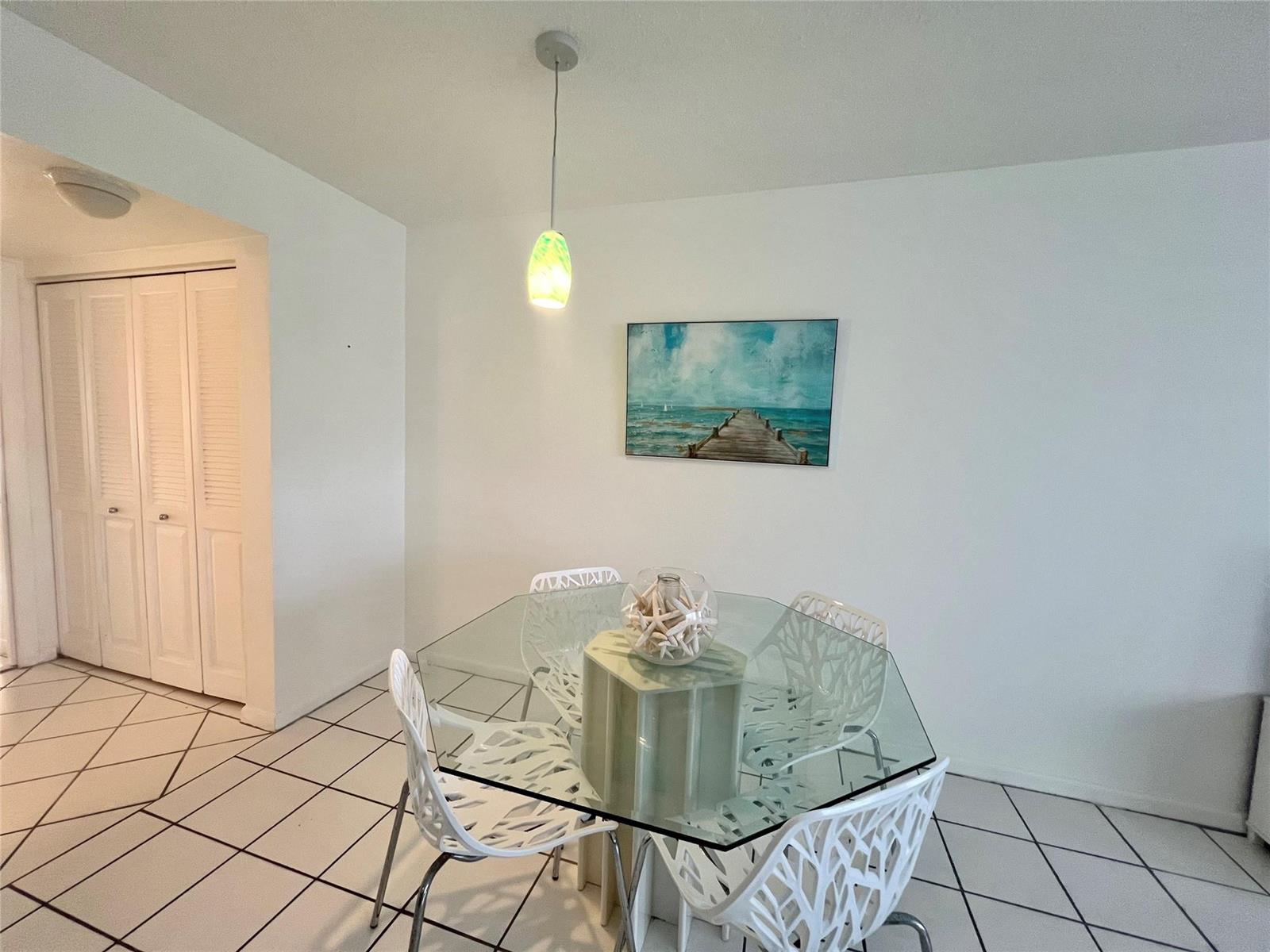 A dining area features a glass-topped table, white patterned chairs, and a coastal wall painting — 266 Oakridge P # 266, Deerfield Beach FL 33442, DEERFIELD BEACH, FL