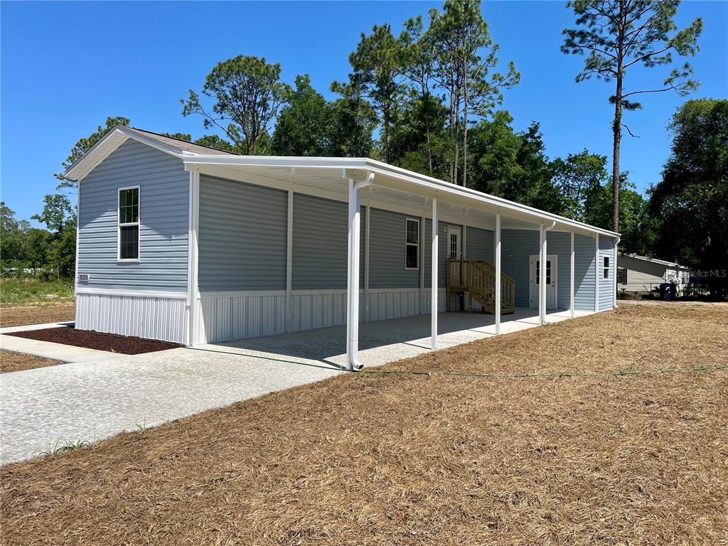 A light blue manufactured home features a long covered carport and a concrete driveway — 11355 NW 12TH LANE, OCALA, FL