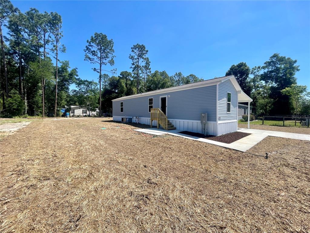 A light blue manufactured home sits on a large, dry, grassy lot under a clear sky — 11355 NW 12TH LANE, OCALA, FL