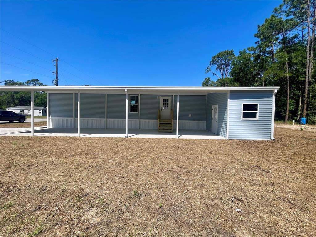 A light blue manufactured home features a covered porch and an attached carport — 11355 NW 12TH LANE, OCALA, FL