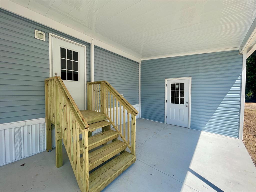 A covered porch with blue vinyl siding, two white doors, and wooden stairs — 11355 NW 12TH LANE, OCALA, FL