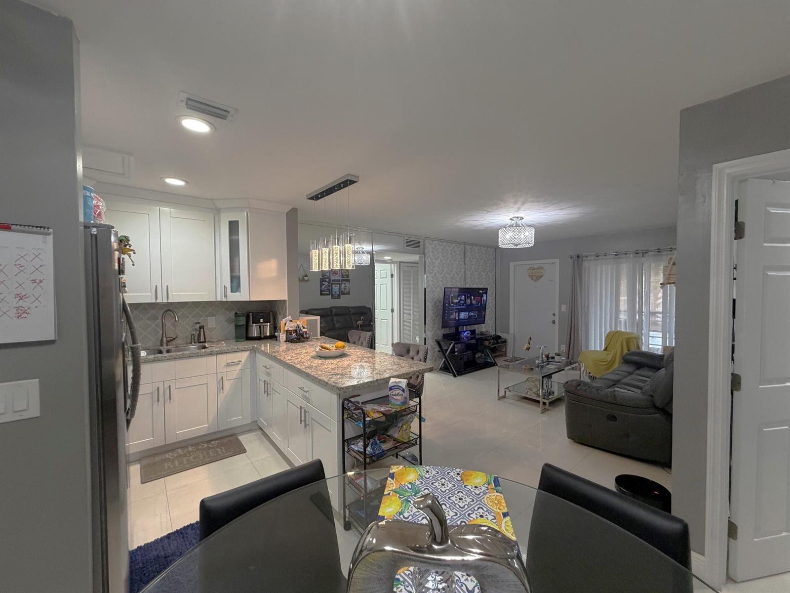 An open-concept kitchen and living area features white cabinetry, granite countertops, and tile flooring — 6575 W 27th Court # 46, Hialeah FL 33016, HIALEAH, FL