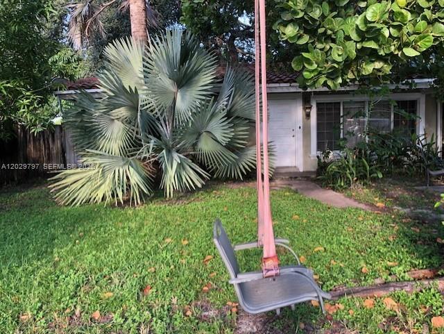 A hanging chair sits on a grassy lawn in front of a house with palm trees — FORT LAUDERDALE, FL