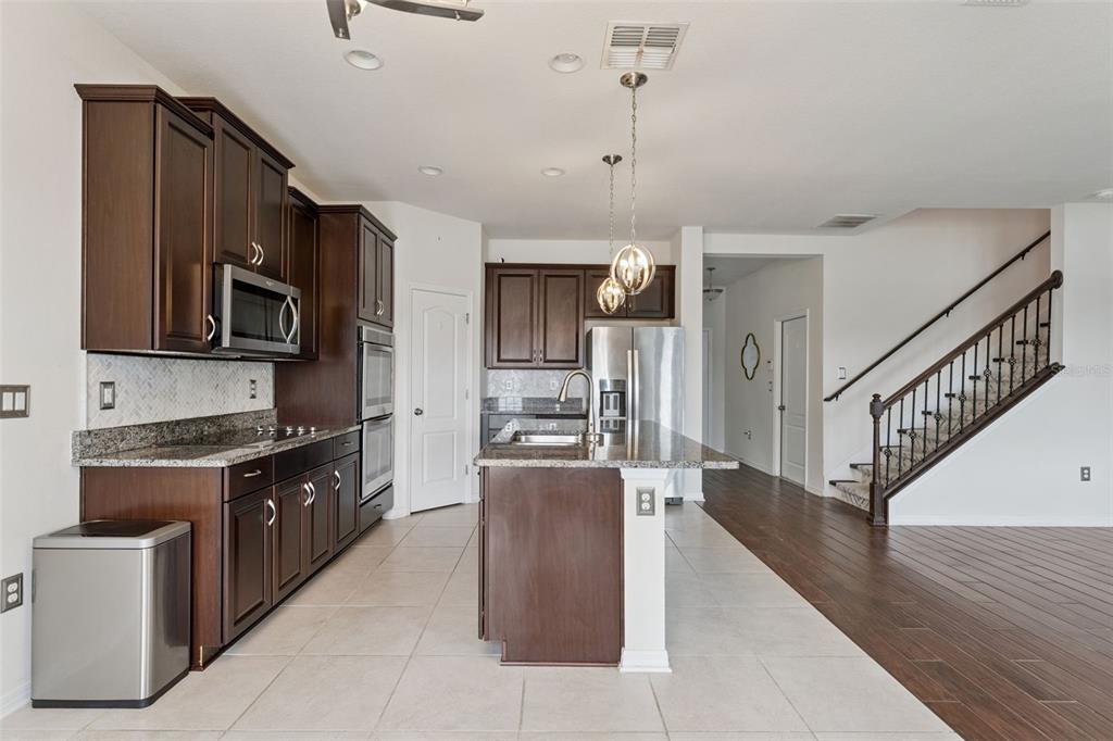 A kitchen features dark wood cabinets, granite countertops, a center island, and tile flooring — 4080 GOLDEN WILLOW CIRCLE, APOPKA, FL