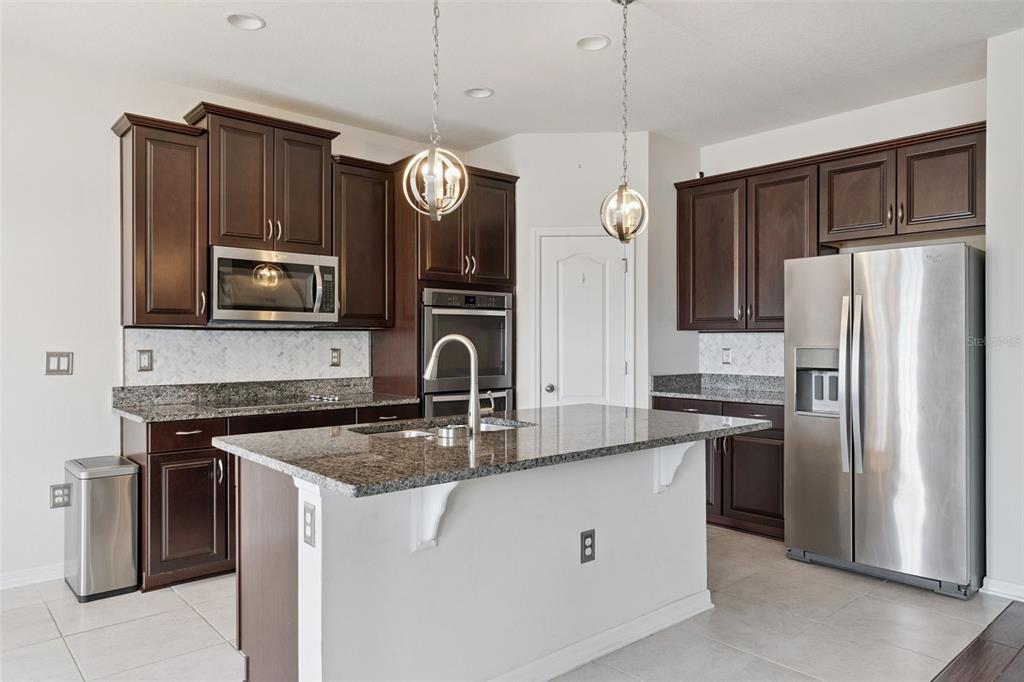 A kitchen features dark wood cabinets, granite countertops, stainless steel appliances, and a central island — 4080 GOLDEN WILLOW CIRCLE, APOPKA, FL