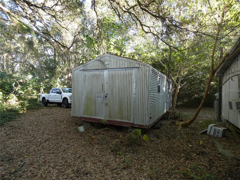 A corrugated metal shed sits on a leaf-covered lot near a white pickup truck — 13701 NE 10TH COURT, CITRA, FL