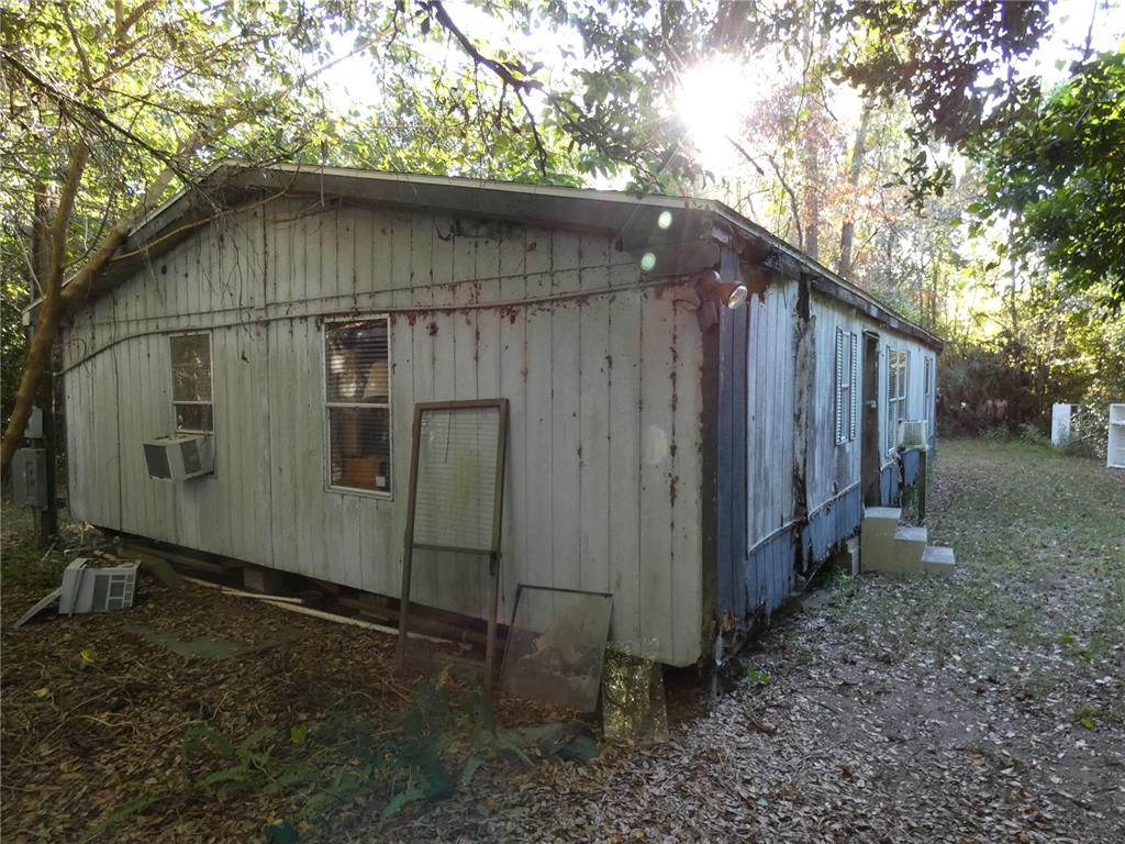 An exterior view of a weathered, single-wide mobile home with peeling siding and window units — 13701 NE 10TH COURT, CITRA, FL