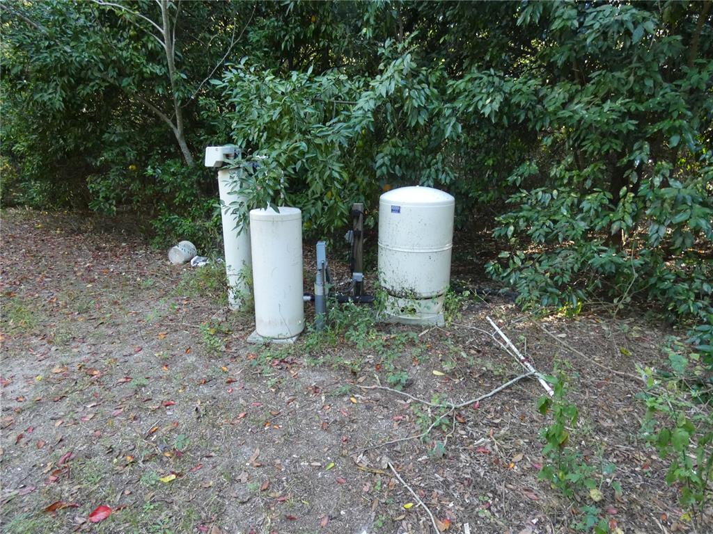 An outdoor well pump system with two white tanks sits in a wooded area — 13701 NE 10TH COURT, CITRA, FL