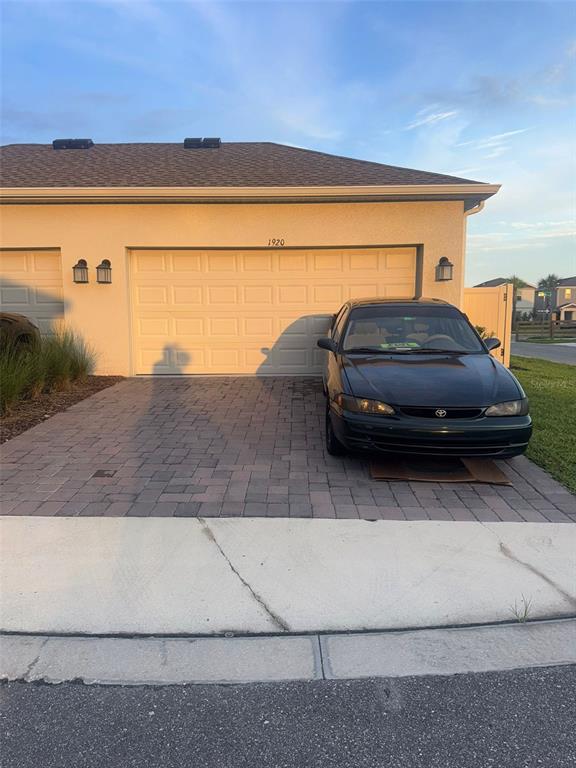 A dark sedan is parked on a paved driveway in front of a house garage — 1920 TOHOQUA BOULEVARD, KISSIMMEE, FL