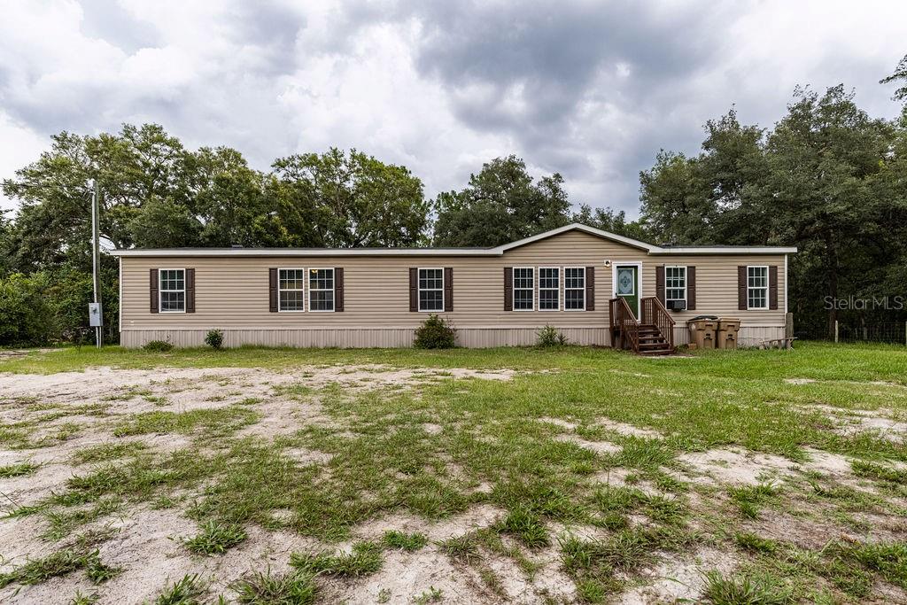 A single-story manufactured home with tan siding sits on a large, grassy lot — 24821 OLD DEER ROAD, PAISLEY, FL